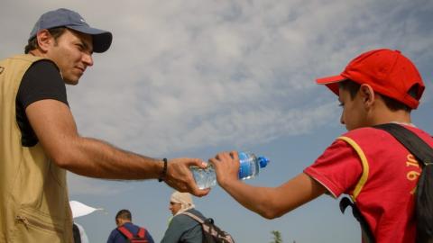 A World Vision staff hands a water bottle to a young man crossing from Serbia into Croatia.