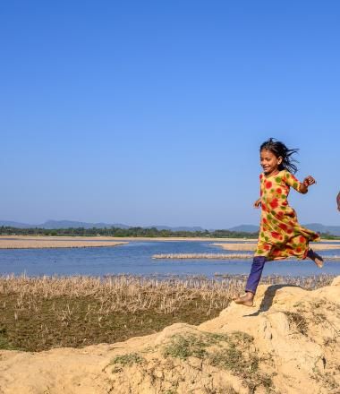Children run along a lake in Bangladesh