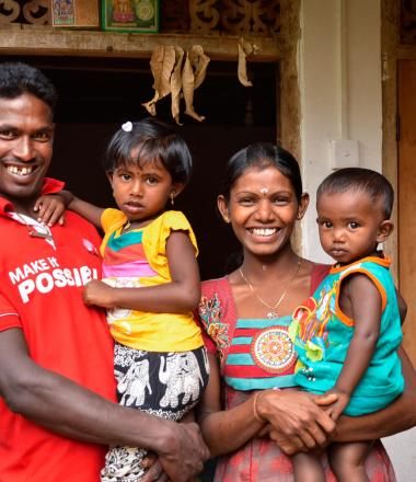 A sri lankan family smiles in front of their home