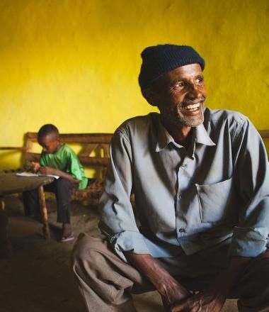 An Ethiopian man in his home with his son reading in the background