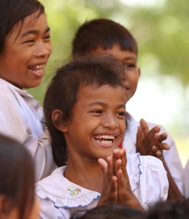 Cambodian girl smiling with student peers around her all clapping their hands with joy.