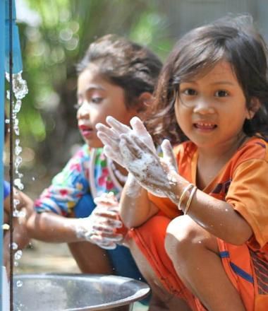 Three Khmer girls wash their hands in a bucket from a tap installed by World Vision Cambodia