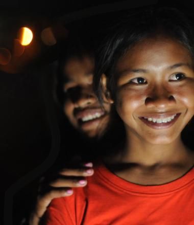 Two young Khmer women stand smiling, it is night time