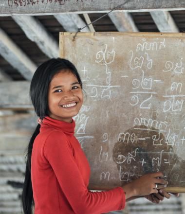 Khmer youth stands in front of blackboard with Khmer script teaching students at youth club, Cambodia