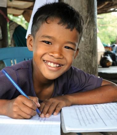 Khmer boy smiles at the camera with pen in hand, writing in his school books, Cambodia.