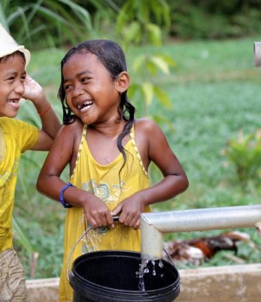 Khmer boy and girl laughing at each other playing in water from pump installed by World Vision Cambodia.