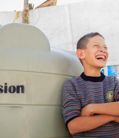 Boy smiling, leaning against water tank