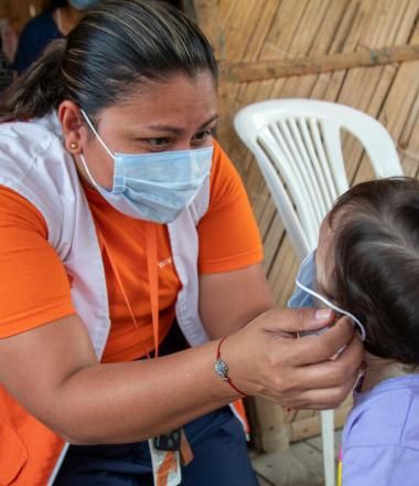 World Vision staff member helps child put on mask
