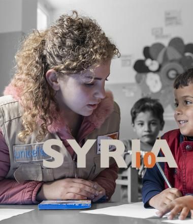 Syria_10 banner_World Vision staff member helps Syrian refugee child in camp in Jordan