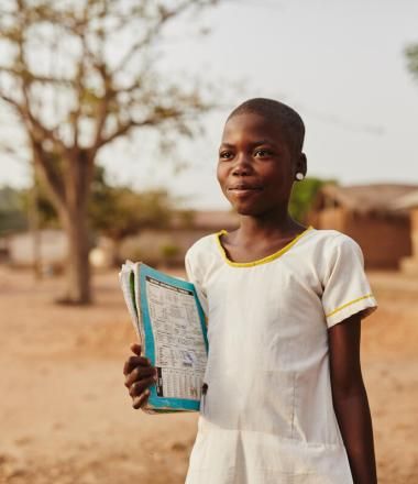 Child in Ghana stands with her school book in hand