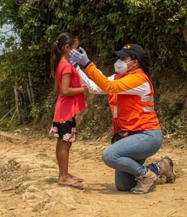 World Vision staff helps child put on mask