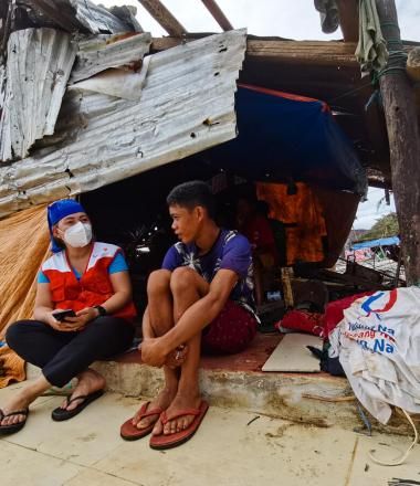 World Vision staff member sits with survivor in the Philippines following the typhon