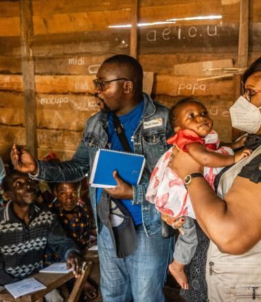 WVI staff speak to villagers inside of a hut