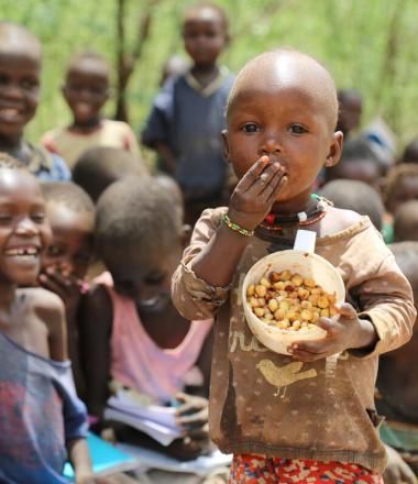 Child eats a bowl food of nuts while other children giggle in the background