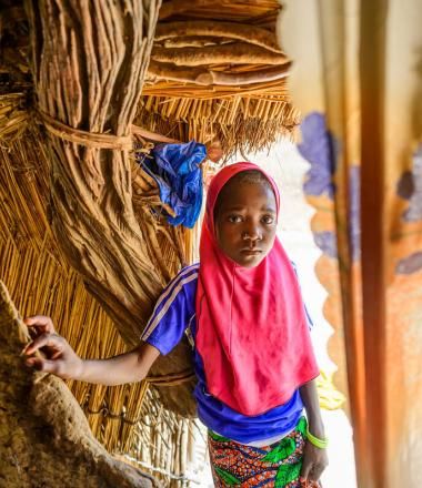 young girl stands inside the entrance to her family's hut