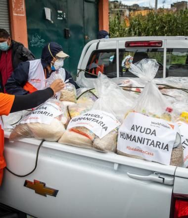 woman distributes packages of food from the bed of a truck