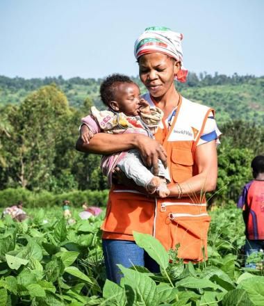 WV volunteer walks through a field holding a baby