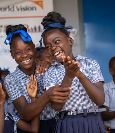 several girls laugh and clap their hands in front of a World Vision sign