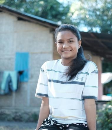 girl sits outside a house smiling