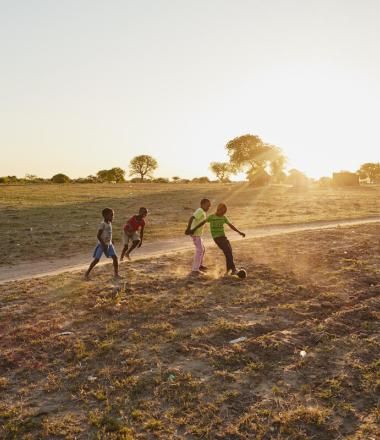 children play futbol in a dirt field