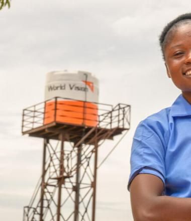 Viola, age 16, stands in front of the water tower at her school, Bulanda Primary School.