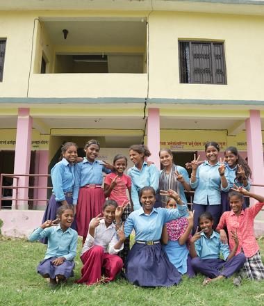 Girl students pose in front of their school.