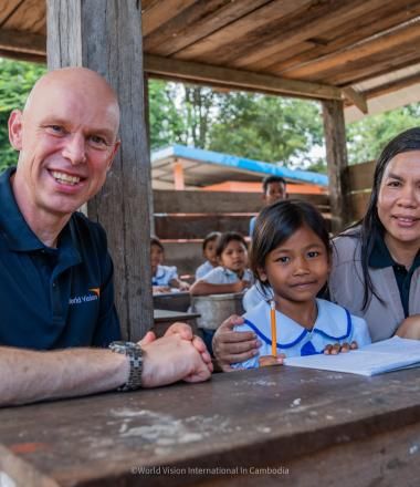 Andrew Morley at desk with child in Cambodia