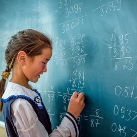 A girl in Mongolia writes on a chalkboard at school