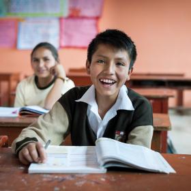 Image shows boy with textbook in school classroom