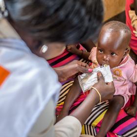 A baby receives a food pouch from a World Vision worker in Africa