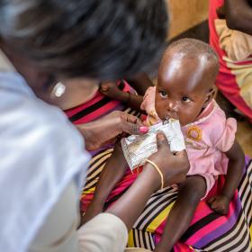 Little girl being fed by World Vision worker