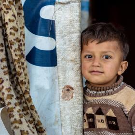 A Syrian boy stands outside his refugee home
