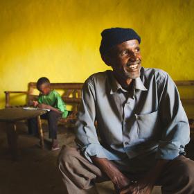 An Ethiopian man in his home with his son reading in the background