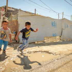 Two boys jumping in puddles at refugee camp