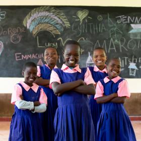 Girls smile while standing in their classroom