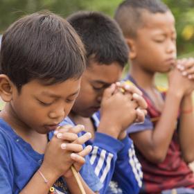Three Khmer boys sitting with their finders locked and their eyes closed praying
