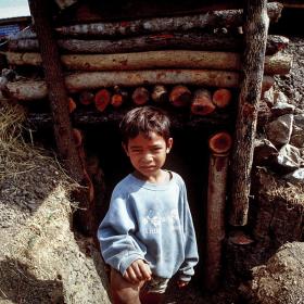 Young Khmer boy stands outside bomb shelter in rural Cambodia province.