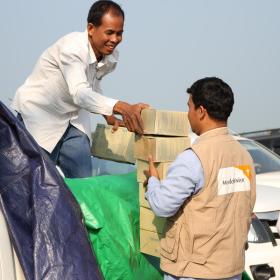 Two men from the World Vision emergency response team unload food supply boxes from the back of a white ute