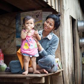 Khmer mother smiles as she holds up her baby toddler so she is standing