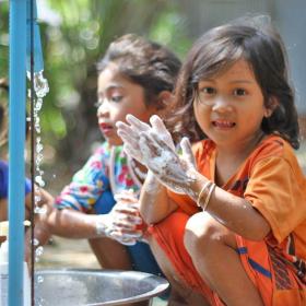 Three Khmer girls wash their hands in a bucket from a tap installed by World Vision Cambodia