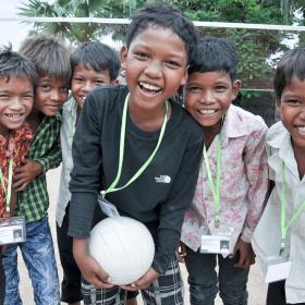 Group of three Khmer boys all smiling and laughing on outdoor volleyball court, Cambodia.