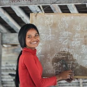 Khmer youth stands in front of blackboard with Khmer script teaching students at youth club, Cambodia