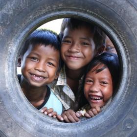 Three Khmer boys poke their heads through an old tire smiling at the camera