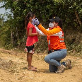 World Vision staff helps child put on mask