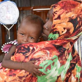 Hunger crsis pic, mother with young child in her arms near scale