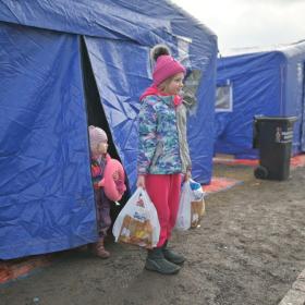 Refugee children stand outside tent shelter