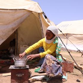 girl sits outside tent mixing food in a pot