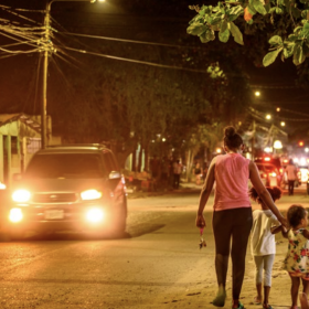 a mother walks her two children down a street at night