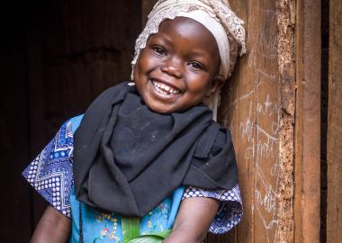 A girl stands against a wall smiling