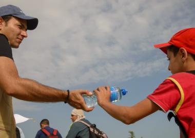 A World Vision staff hands a water bottle to a young man crossing from Serbia into Croatia.